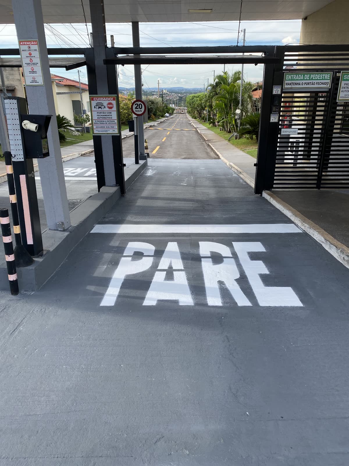 Acesso de condomínio com a palavra PARE e linha de retenção pintadas no piso